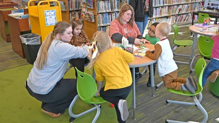 Adults and children engaging in art activities together at a library table during an early intervention program in Sandusky County, Ohio