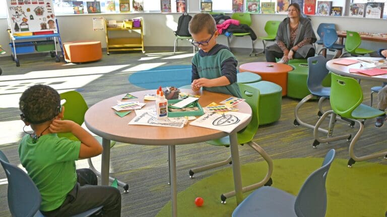 Children engaging in art activities at a colorful classroom table with a teacher supervising in Sandusky County developmental disability services facility