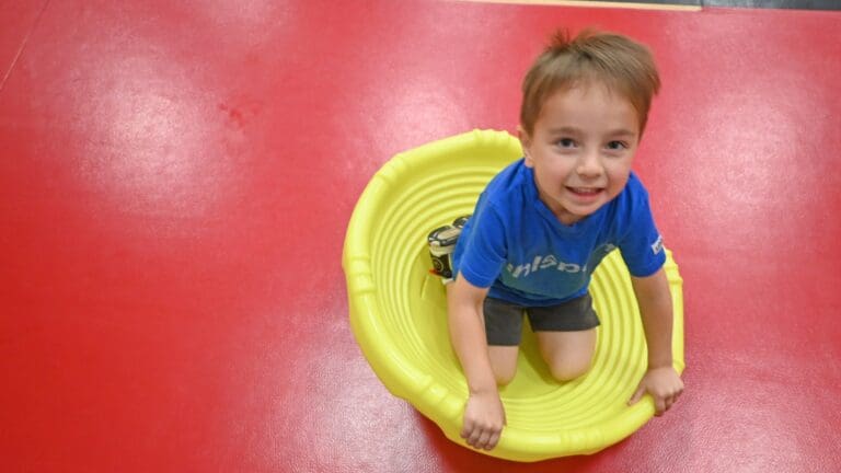 Young child crawling through a yellow tunnel on a red padded floor surface during early intervention activity