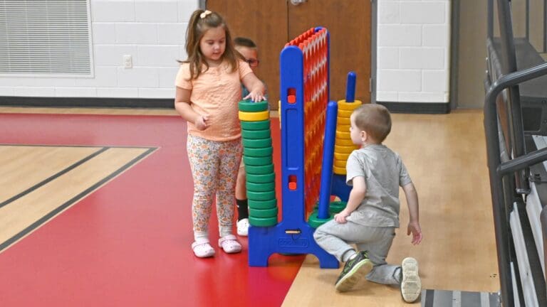 Children playing with colorful stacking rings and building blocks in a gymnasium during early intervention activity at School of Hope in Sandusky County