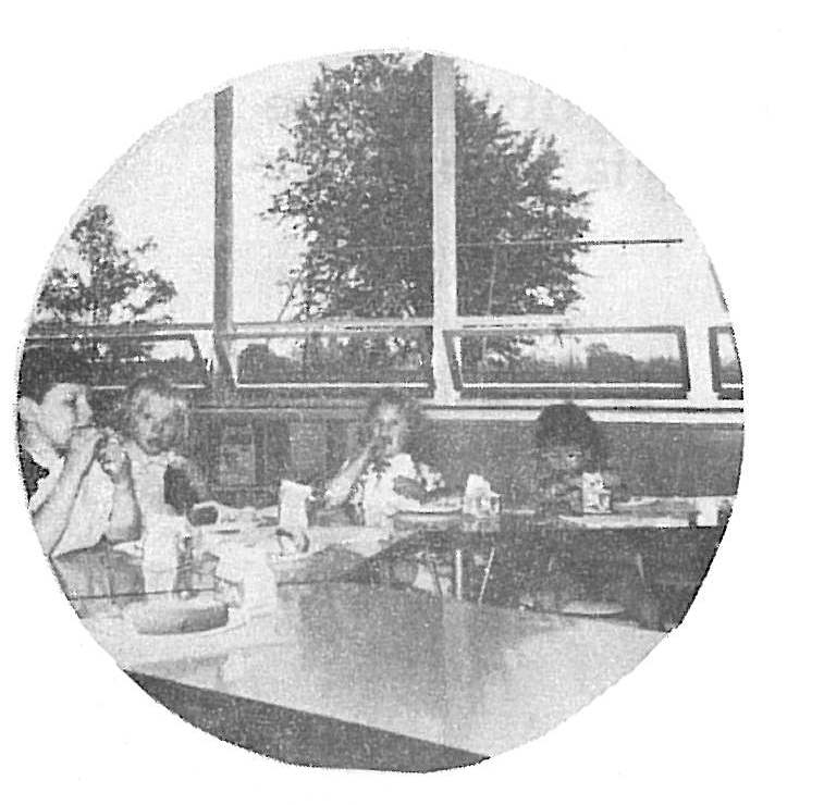 Black and white photograph of several people seated at a table during a meeting or meal, with large windows showing trees in the background, likely from a developmental services facility in Sandusky County Ohio